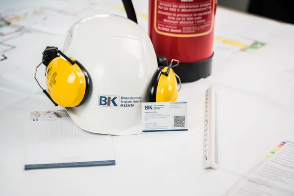 Bauhelm, Feuerlöscher und Baupläne auf einem Planungstisch